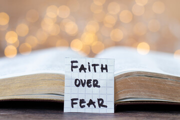 Faith over fear, handwritten quote and open holy bible book with bokeh light background. Christian...