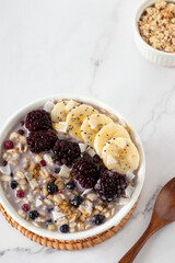 Healthy breakfast oatmeal bowl with oat flakes, chia seeds, banana, and berries on white marble table. Top view. Eating sustainable vegan food concept.