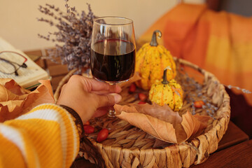 Glass of red wine on wooden table decorated with pumpkins, books and dried leaves outdoor. Woman's hand holding wineglass. Autumn composition for Thanksgiving. Autumnal mood