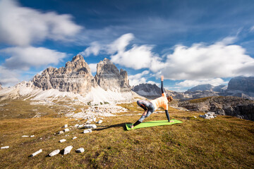 A woman practising yoga with the view to the monumental peak of Three Peaks of Lavaredo/Tre Cime di...