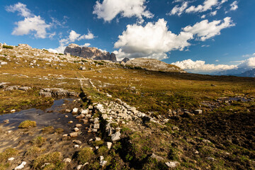 Rocky footpaths below the monumental peak of Tre Cime with the cloudy blue sky