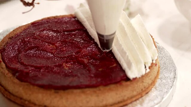 the pastry chef decorates the cake with a piping bag and whipped cream
