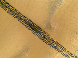 Bird's eye view of the sandy shore, long shadows on the sand from the wooden poles of the breakwater

