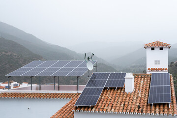 Sustainable living in a fog-covered mountain village, with solar panels on terracotta rooftops harnessing renewable energy - obrazy, fototapety, plakaty