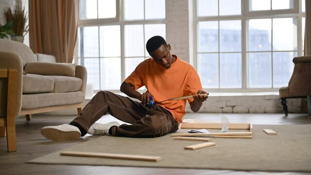 A young black guy measures parts with a tape measure to check their compatibility for assembly.