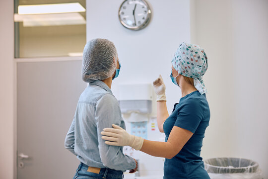 Rear view of ophthalmologist and her patient looking at time on clock after eye surgery at clinic.