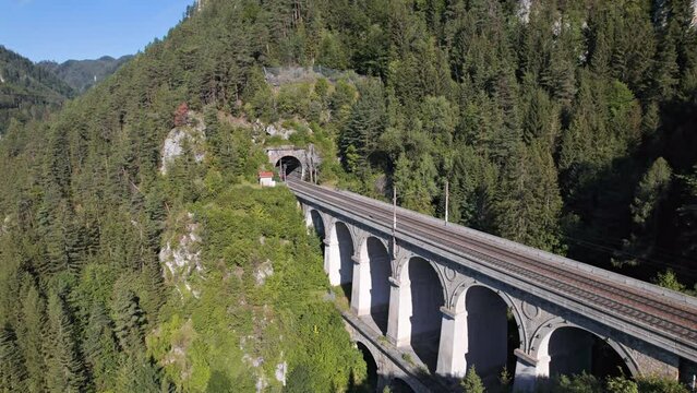 Aerial view of red passenger train rides on Krauselklause Viaduct on historical Semmering mountain railway (Semmeringbahn), Lower Austria.