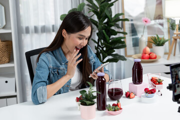 Smiling young beautiful Asian reviewing tasty mixed strawberry and cherry juice detox drinks,...