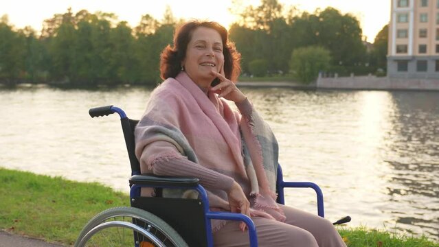Happy senior woman in wheelchair smiling enjoying freedom walking on road in city park outdoor. Old cheerful positive woman in chair for people with disability. Disability disease rehabilitation