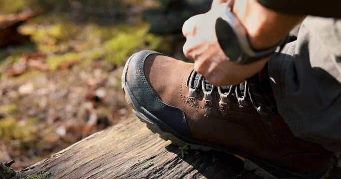 man tying hiking boot shoelace on fallen tree trunk. outdoor footwear and clothing