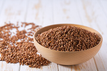Organic buckwheat in a wooden bowl on a white wooden table.