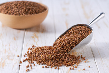 Raw buckwheat in a metal scoop on a white wooden table.