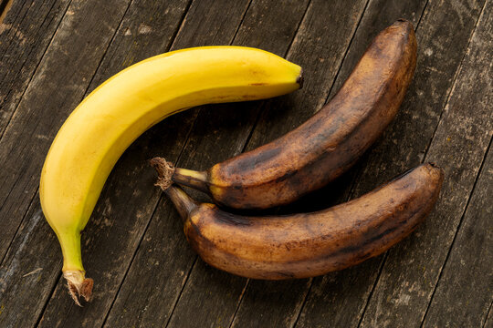 Two overripe bananas and one ripe lying on a rustic wooden garden table.  Top view.