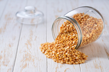 Raw dried peas spill out of a glass storage jar on a white wooden table.