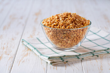 Raw dried peas in a glass plate on a white wooden table.
