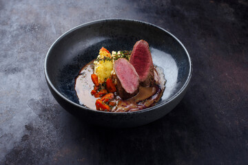Traditional fried venison back filet with kaki fruit, carrots and potato puree in game sauce served as close-up on Nordic design plate
