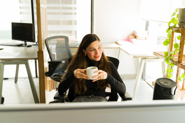 Beautiful Hispanic woman relaxing at the office and enjoying a cup of coffee