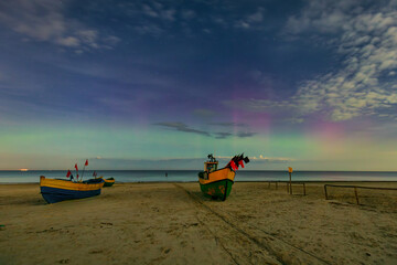 Northern lights over the Baltic Sea beach in Jantar with fishing boats, Poland. - 767375261