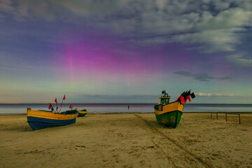Northern lights over the Baltic Sea beach in Jantar with fishing boats, Poland. - 767375277