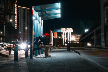 Persona esperando en la parada del transporte por la noche - obrazy, fototapety, plakaty