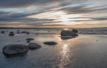 Fototapeta na wymiar Andineeme Estonia - March 25 2024: Southern coast of the Finnish Gulf. Smooth transparent reflective water and granite rocks. Golden hour. Orange sunset markings under the low altitude clouds. 