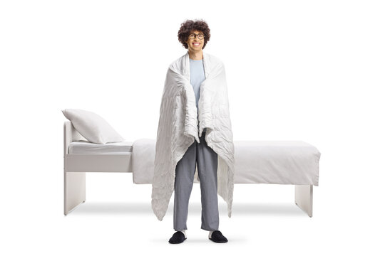 Young man in pajamas wrapped in a blanket standing next to his bed
