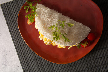 Tapioca Pancake with eggs Brazilian manioc food in front view inside a red ceramic plate