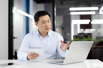 Asian business man watching training video course online, man inside office at workplace writing in...