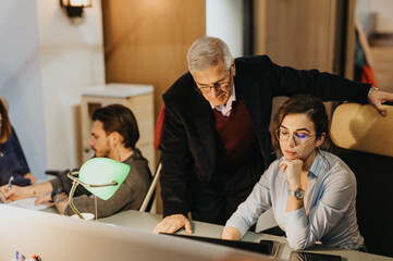 Cross generational business professionals collaborate in a late-night office meeting, analyzing,...