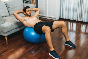 Athletic and sporty man doing situp on fitness ball during home body workout exercise session for fit physique and healthy sport lifestyle at home. Gaiety home exercise workout training concept. - obrazy, fototapety, plakaty