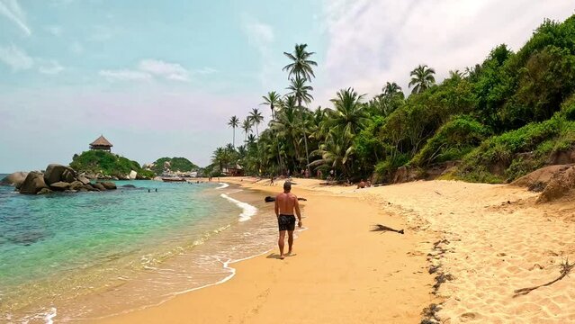 A man walking on the sand in a paradisiacal beach with palms and turquoise water, in the tayrona national park in colombia