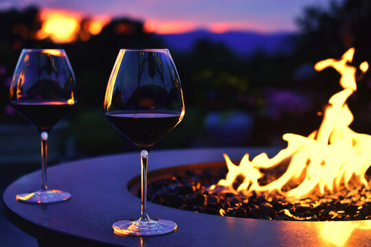Two glasses of red wine by the flames of a fire table firepit right after sunset.