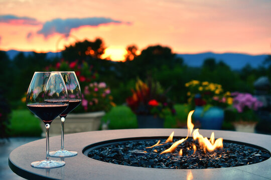 Two glasses of red wine by the flames of a fire table firepit right after sunset.