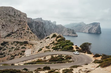 Wandcirkels aluminium Lonely small white car driving by serpentine curved asphalt mountain road near Lighthouse of Cap de Formentor with beautiful seascape with rocky coast. Mallorca Island, Balearic Islands, Spain. © Soloviova Liudmyla