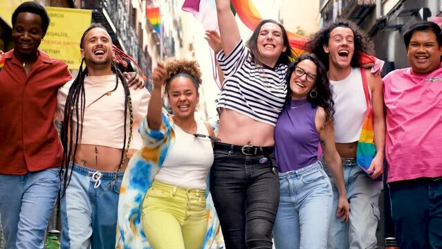 A group of people are holding rainbow flags and laughing at Pride Parade. Scene is happy and celebratory.