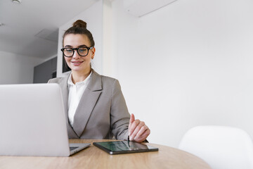 A composed and content professional works on a laptop and interacts with a tablet in a minimalist, clean office environment.