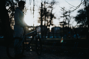 A serene setting as a man stands with his bicycle in a park, surrounded by the beauty of nature at twilight.