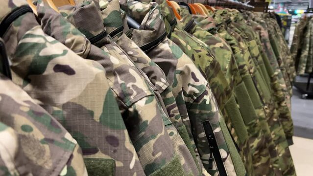 Military camo uniforms of various colors and patterns displayed hanging on racks in a store.