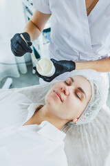 A young woman is sitting at a beautician's appointment, a dermatologist applies a mask to the client's face