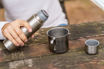 Close-up of hands as a man seated at a mountain table pours coffee, a well-deserved break after a hike..