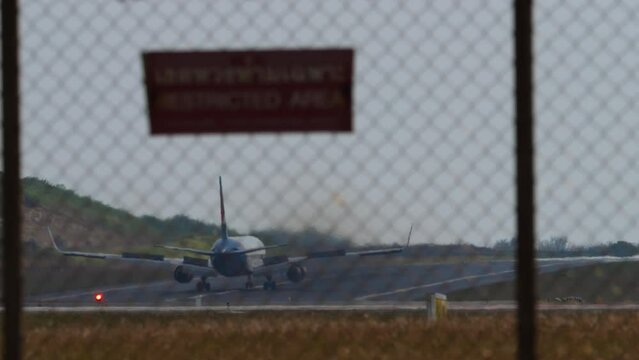 Airplane unrecognizable livery landing and braking, spoilers up. View through the fence. Red sign Restricted area