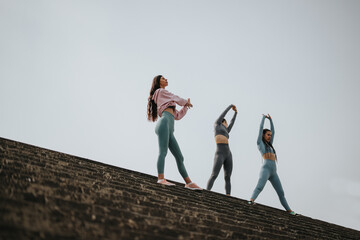 Three women engage in a fitness session, stretching together on a rooftop, exuding energy and...