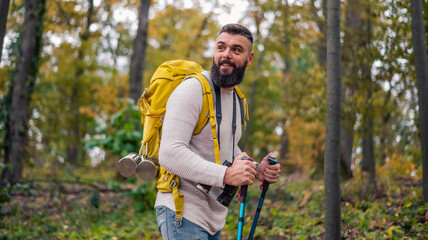 In the midst of an autumn hike, a bearded man, a hiker with a backpack and hiking poles, explores the woodland landscape.
