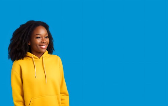 Mujer afroamericana joven y sonriente, con pelo afro y sudadera amarilla sobre fondo azul brillante 