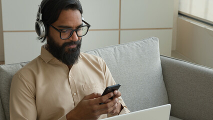 Muslim arabian man in headphones listen audio podcast music on mobile phone Indian guy businessman...