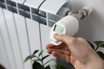 person sets the heating temperature on an electronic thermostat with his hand. Stylish white...
