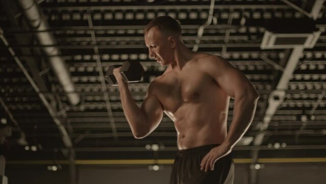 Barechested man lifting dumbbell in gym, showcasing strong muscles