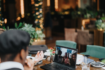 Multiethnic business group engaged in a video call with remote teammates from a warm, inviting restaurant setting.