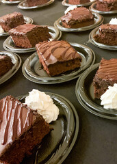Pieces of chocolate cake on plastic plates with whipped cream
