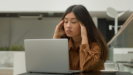 Exhausted overworked Asian chinese japanese woman student girl studying online with laptop in cafe...